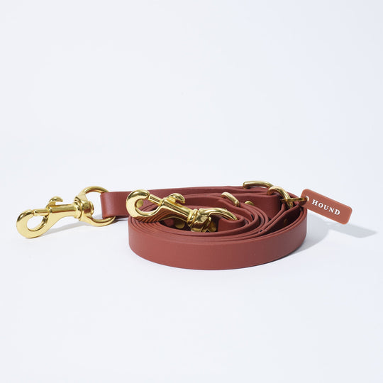 A beautiful saddle coloured HOUND Collection's Crossbody  Leash lays on a white background, with bright equestrian solid brass hardware. 